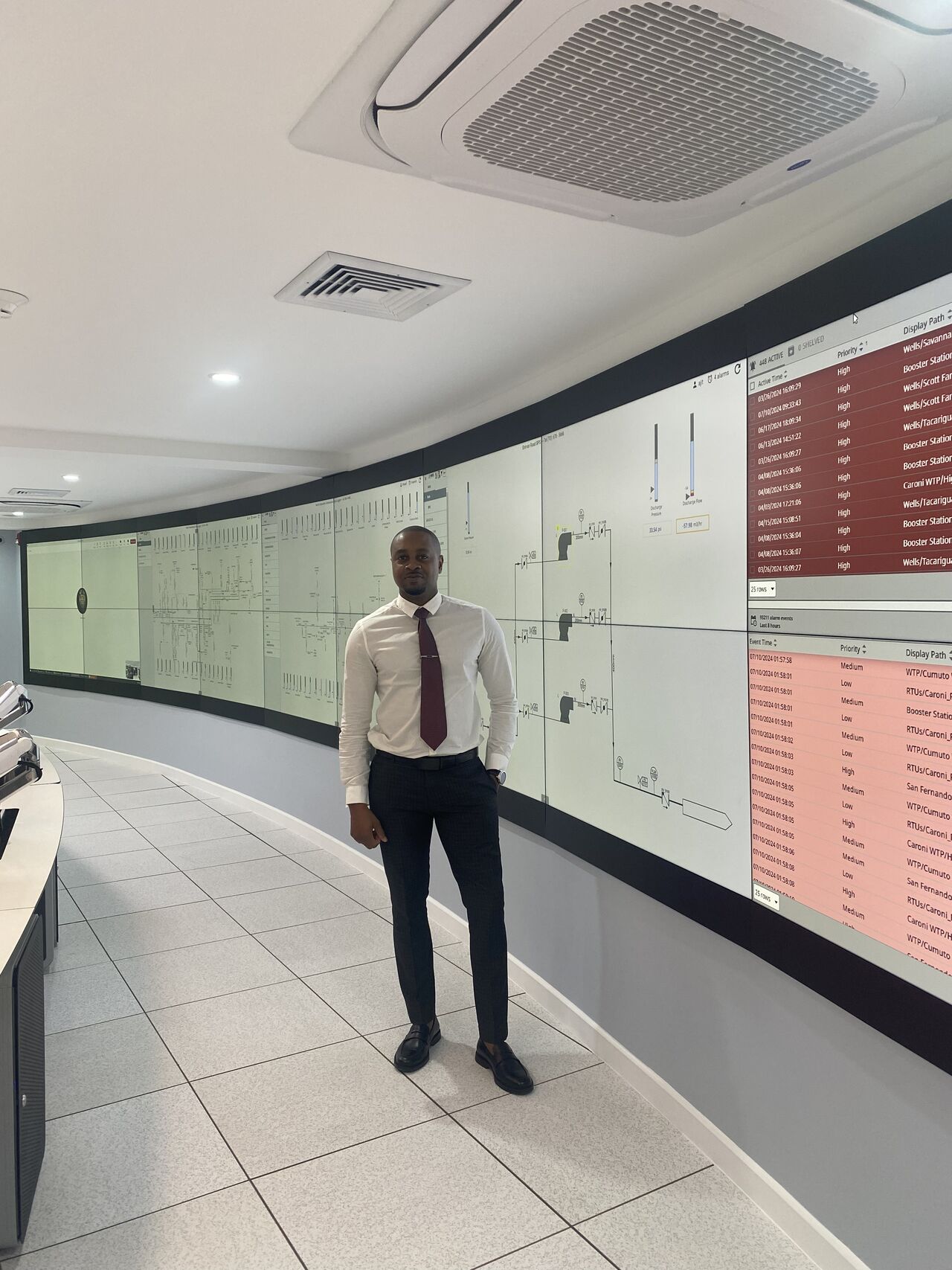 Dane Sandy in an operations control centre in front of a curved wall of live SCADA alarm tables and process diagrams
